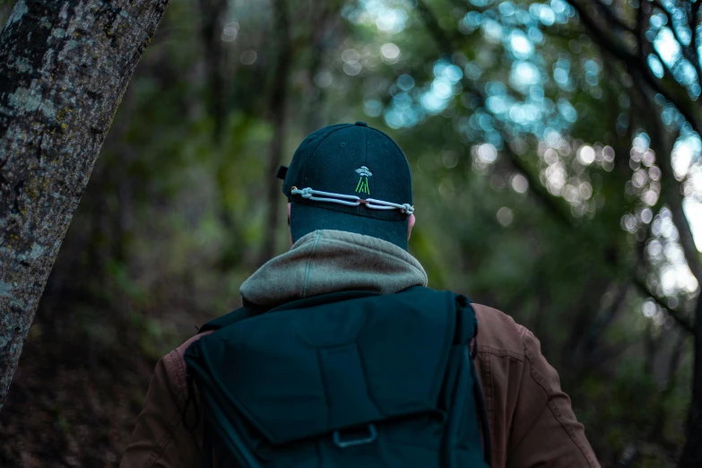 the back end of a man's hat as he walks through a forest