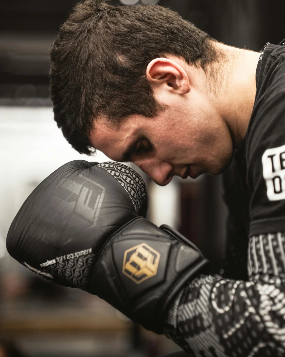 man with black shirt and black boxing gloves looking down