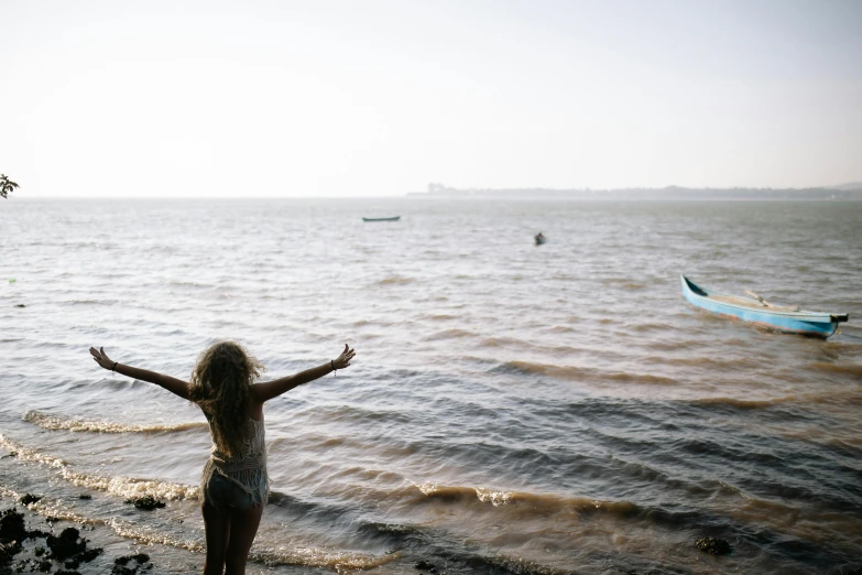 girl with her arms outstretched standing by the water