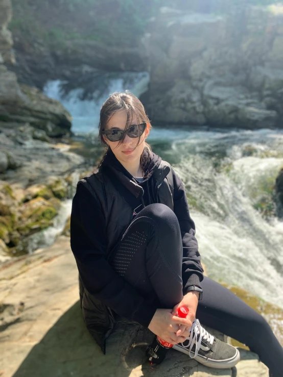 a girl sitting on the edge of a cliff next to a stream