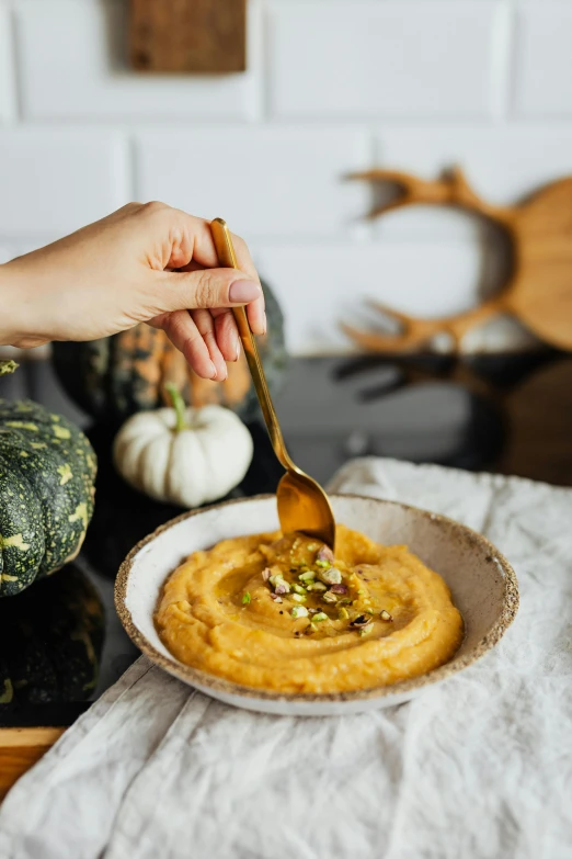 a person eating mashed pumpkin hummus in a white bowl