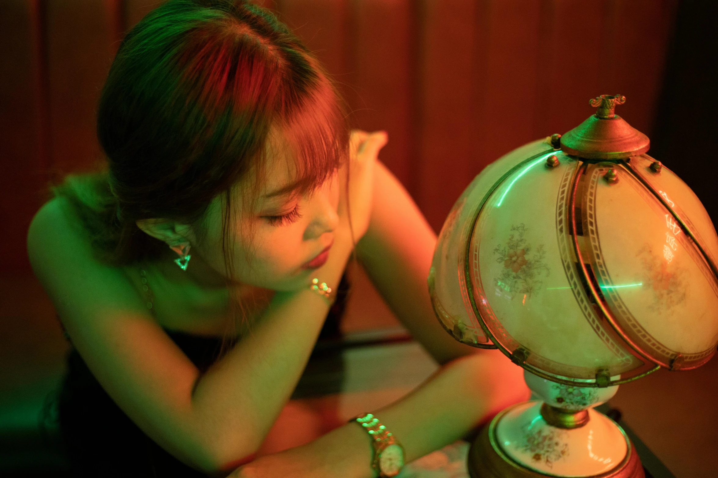 a girl sitting near an old table looking at an antique style light