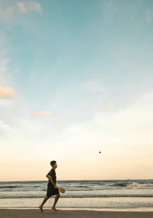 a woman in a long black dress is standing on the beach near water