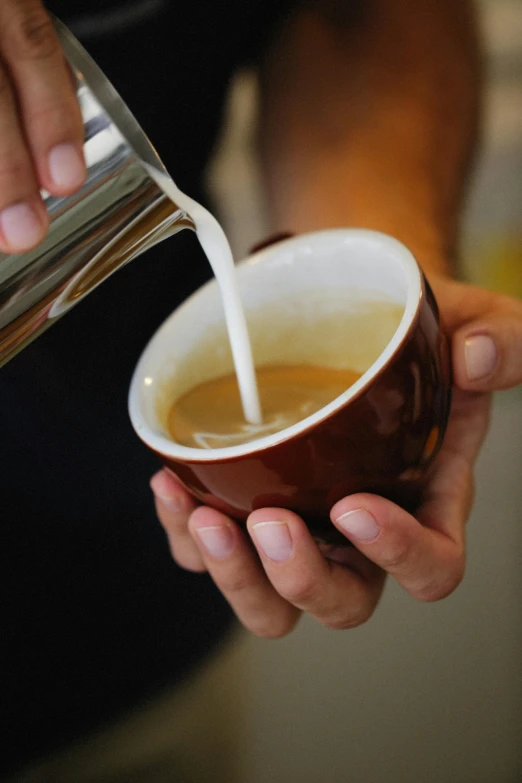 a person pouring soing into a cup filled with coffee