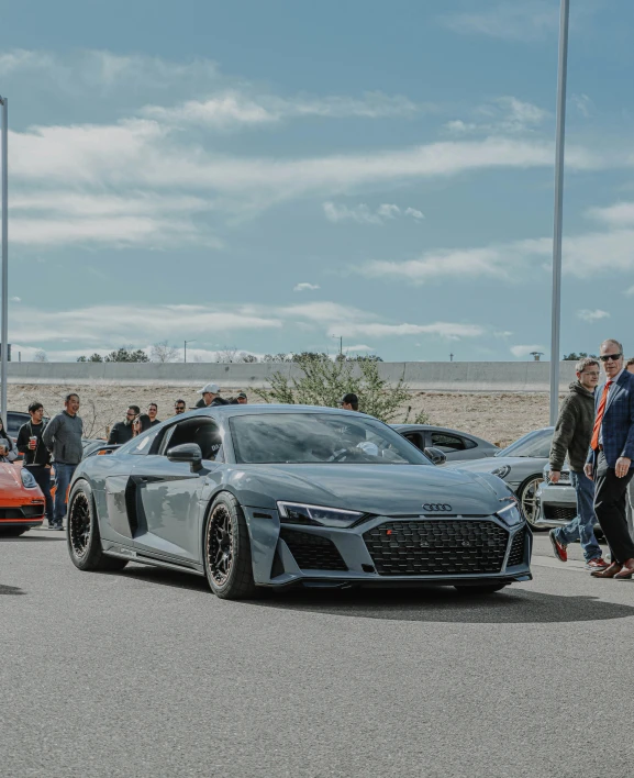 people stand in the parking lot of an automobile show