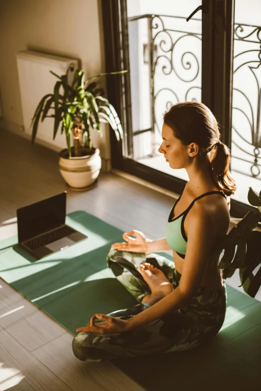 a woman sitting in yoga pose using her phone and laptop