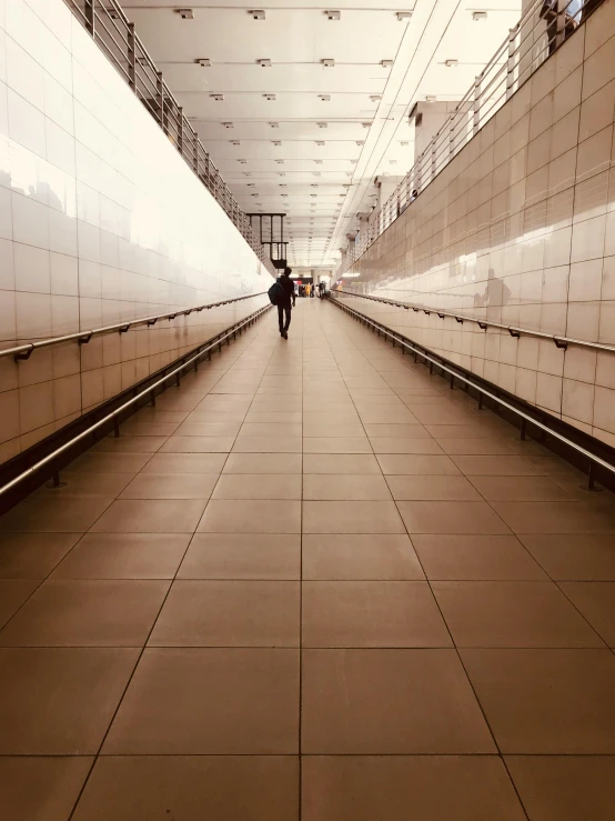 a woman walks down a long narrow walkway between tiled walls