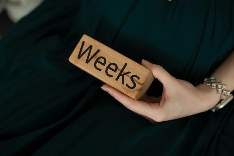 a woman wearing a black dress is holding a block that reads weeks