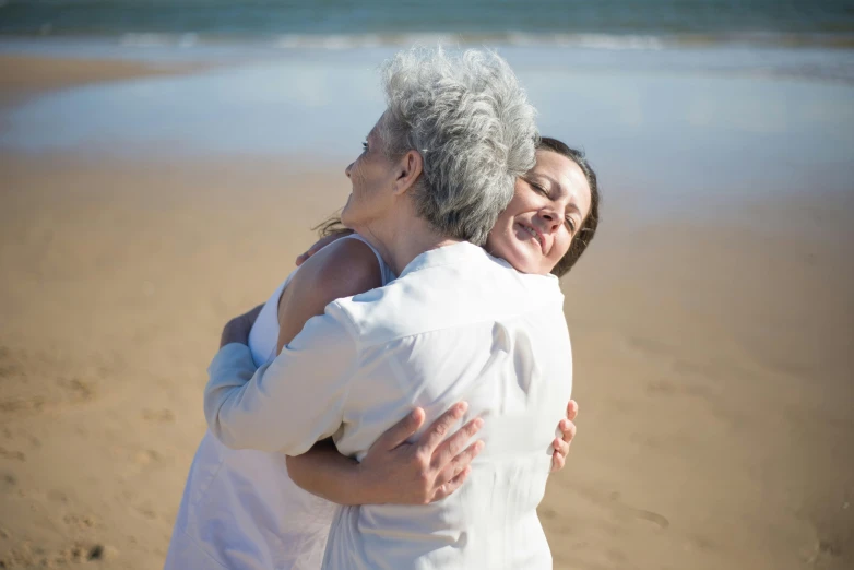 two women hug each other as they stand on the sand