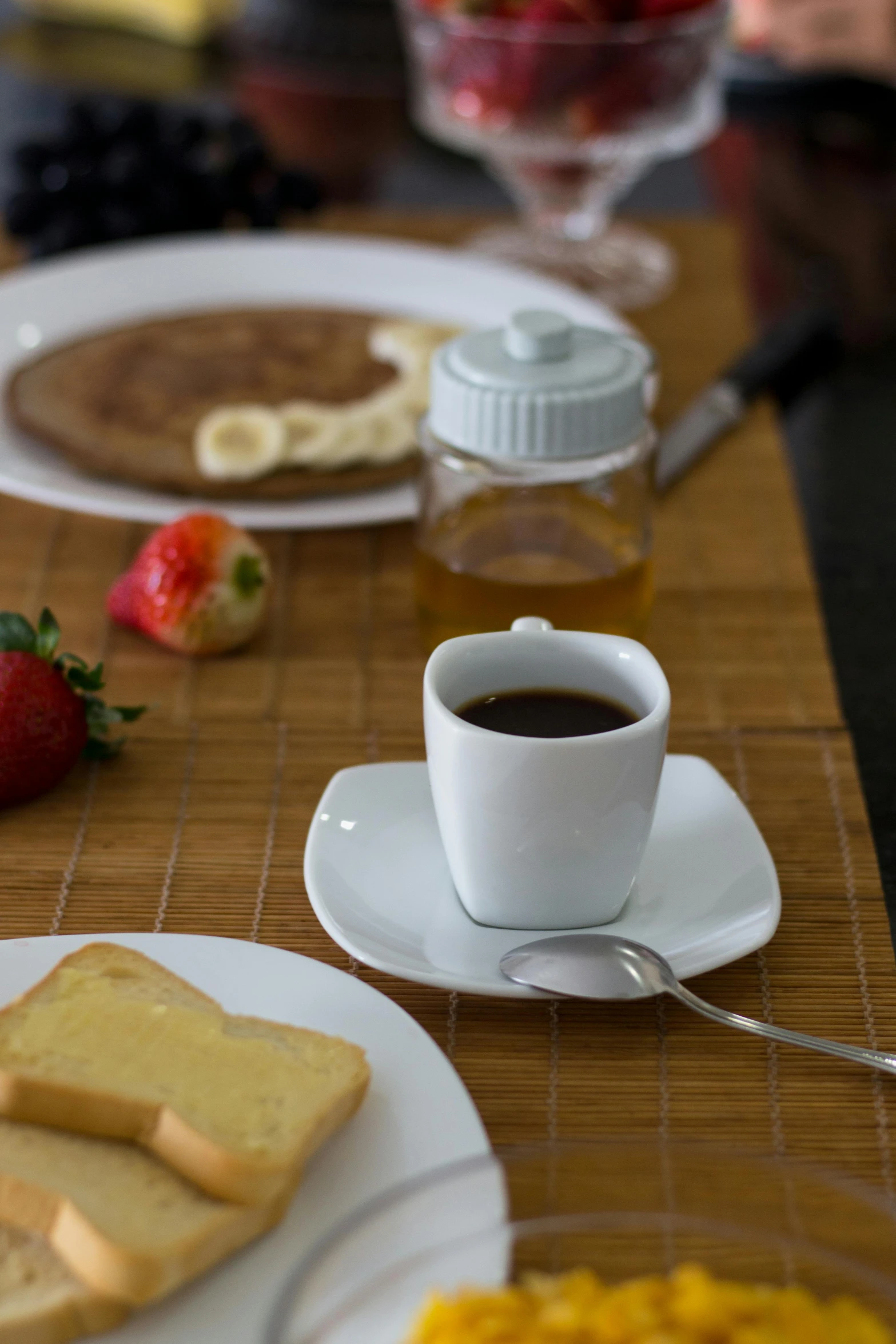 a breakfast meal on a bamboo mat and next to glasses with coffee, fruit, and strawberries