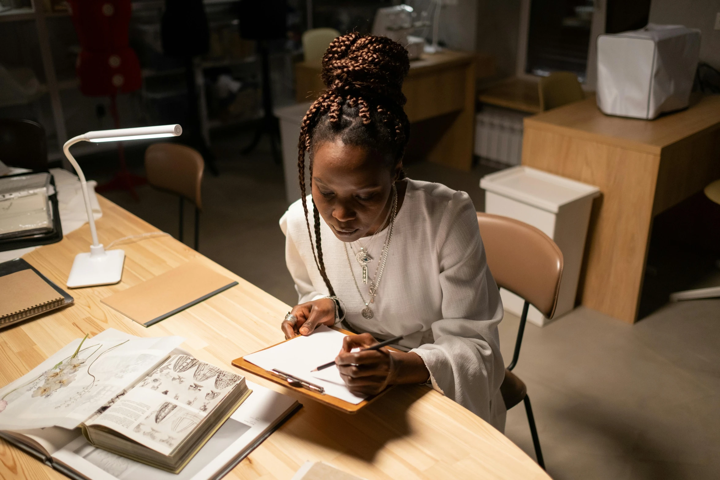 a woman sitting at a desk writing with an open book in front of her