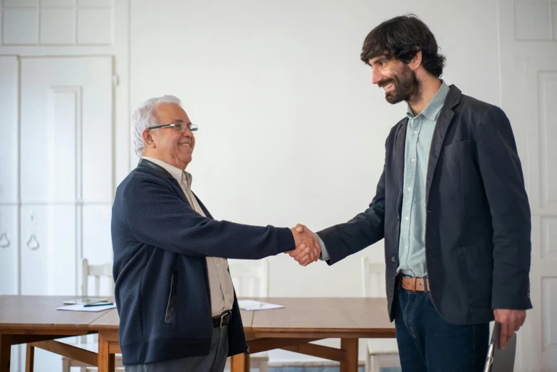 an old gentleman shakes the hands of a man in a suit