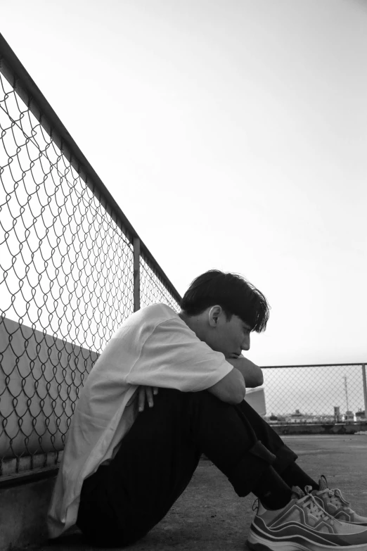 a young man sitting on the ground next to a fence