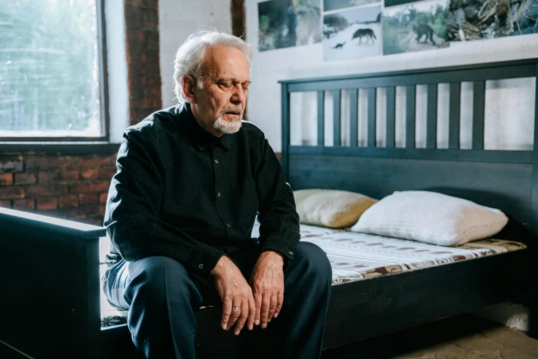 an older man sitting on the edge of his bed