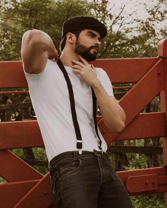 man standing by a red fence in jeans and a white shirt