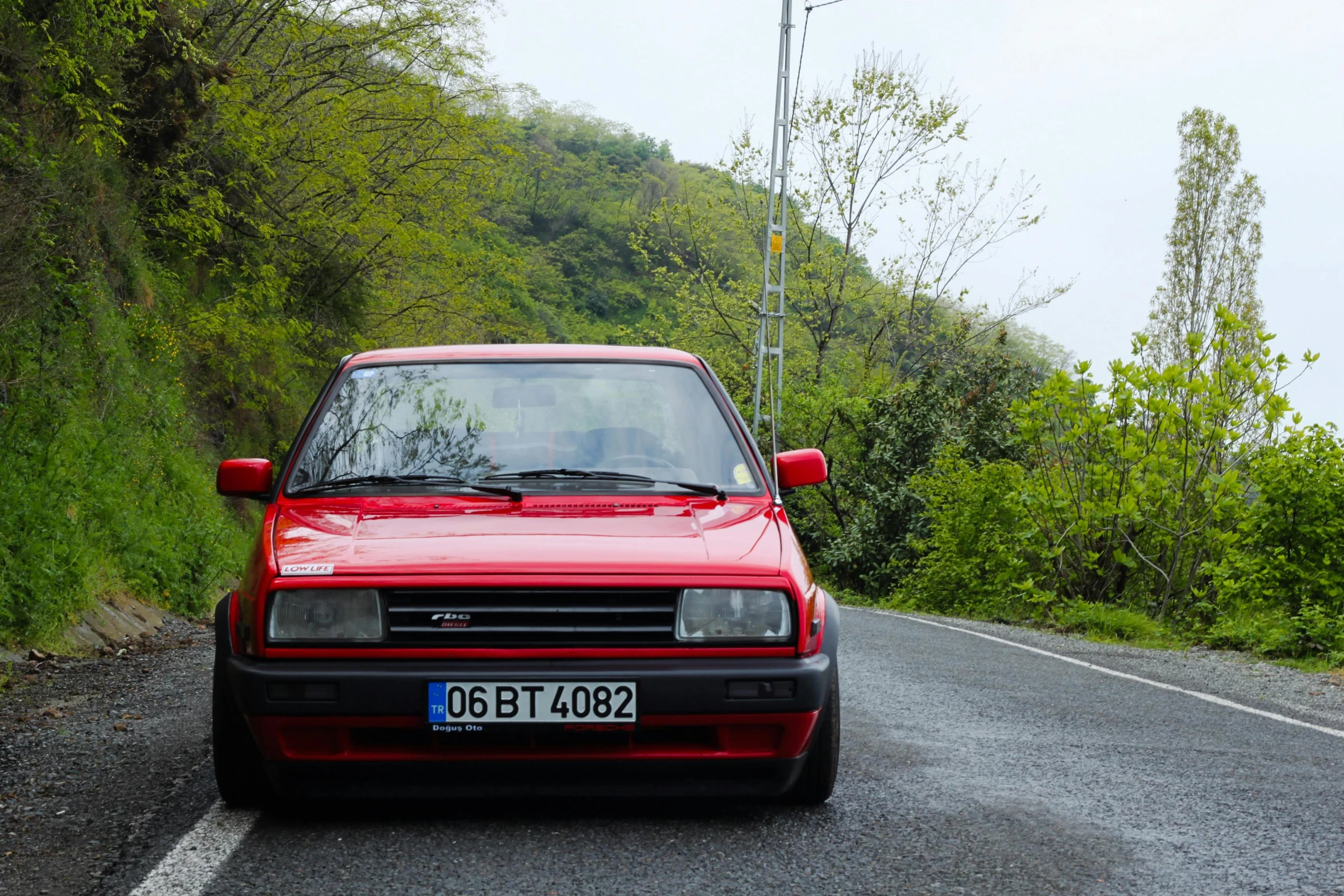 the red car is parked in front of the trees