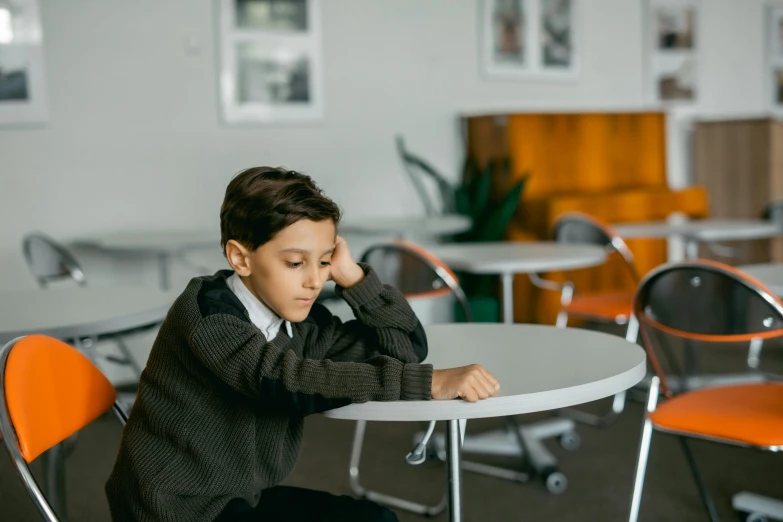 a boy sitting at a table with his hand on his chin