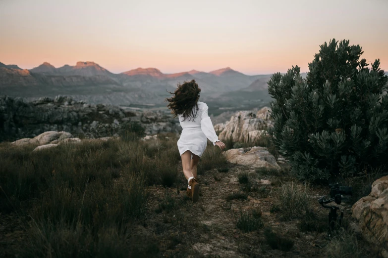 a woman in a dress walking on top of a grass covered field