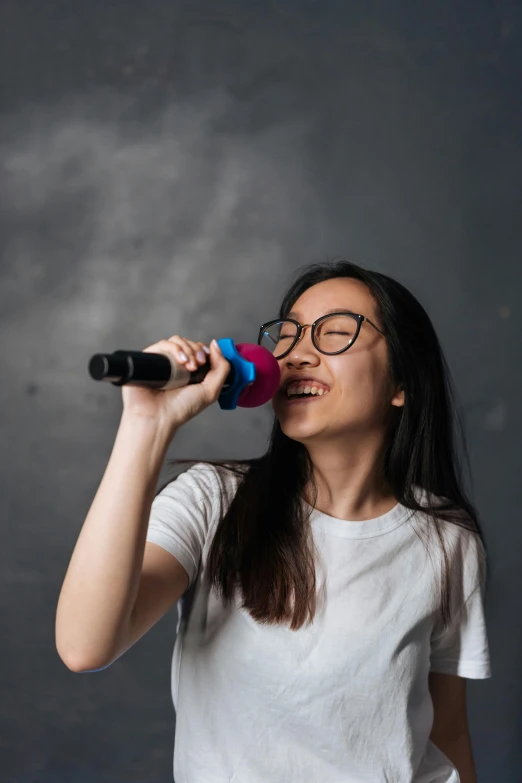 a woman in glasses, with black and pink hair, smiles while holding a microphone