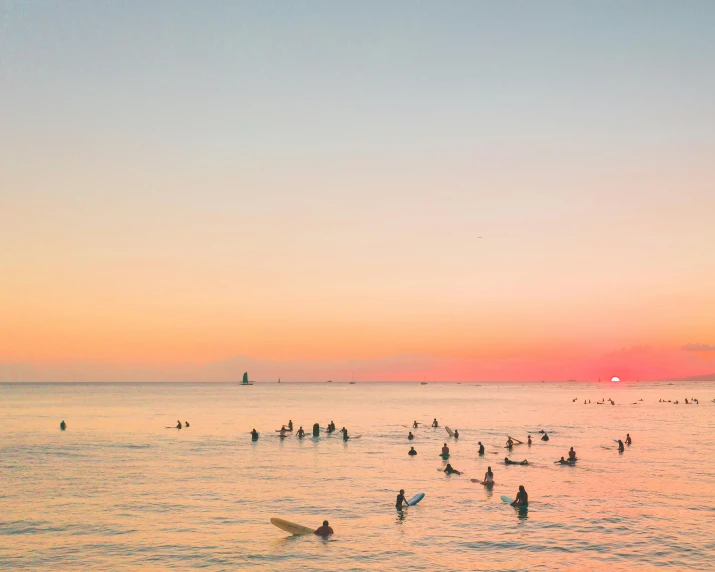 the sky is lit with oranges, oranges and pinks while some surfers are out in the water at sunset