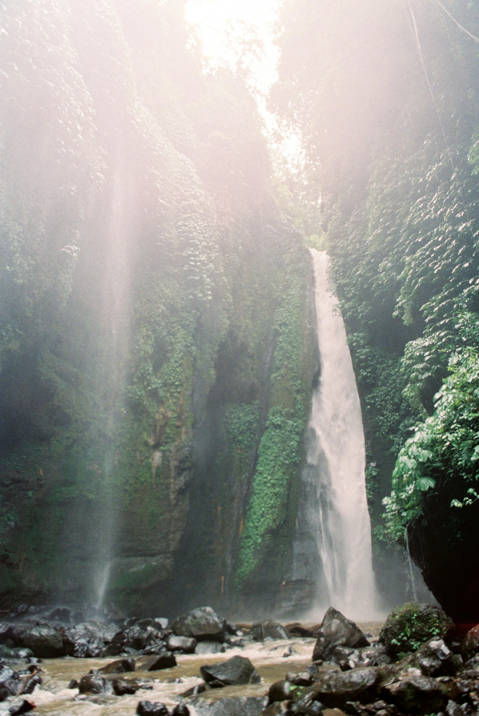 a long waterfall next to a forest in the rain