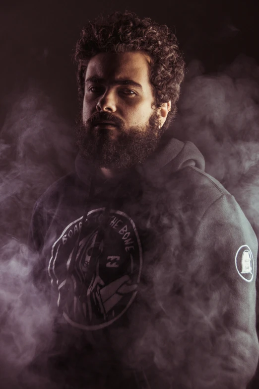 a man standing in smoke wearing a hoodie with an emblem on it
