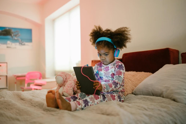 little girl wearing headphones sitting on a bed