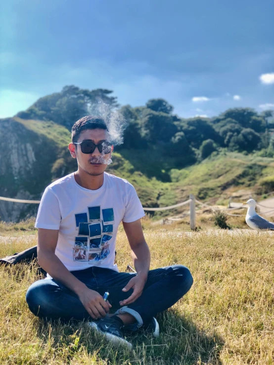 a man sits in the grass in front of a mountain