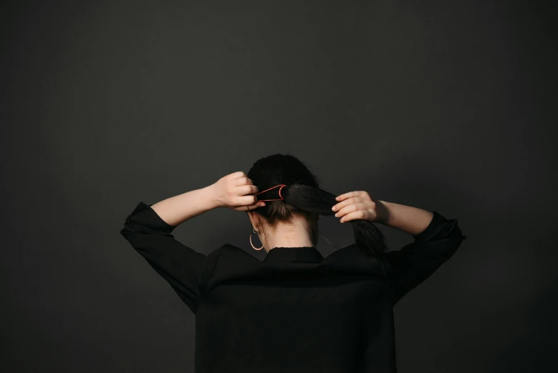 a woman in black holding her hair back and covering the top of her head with her hand