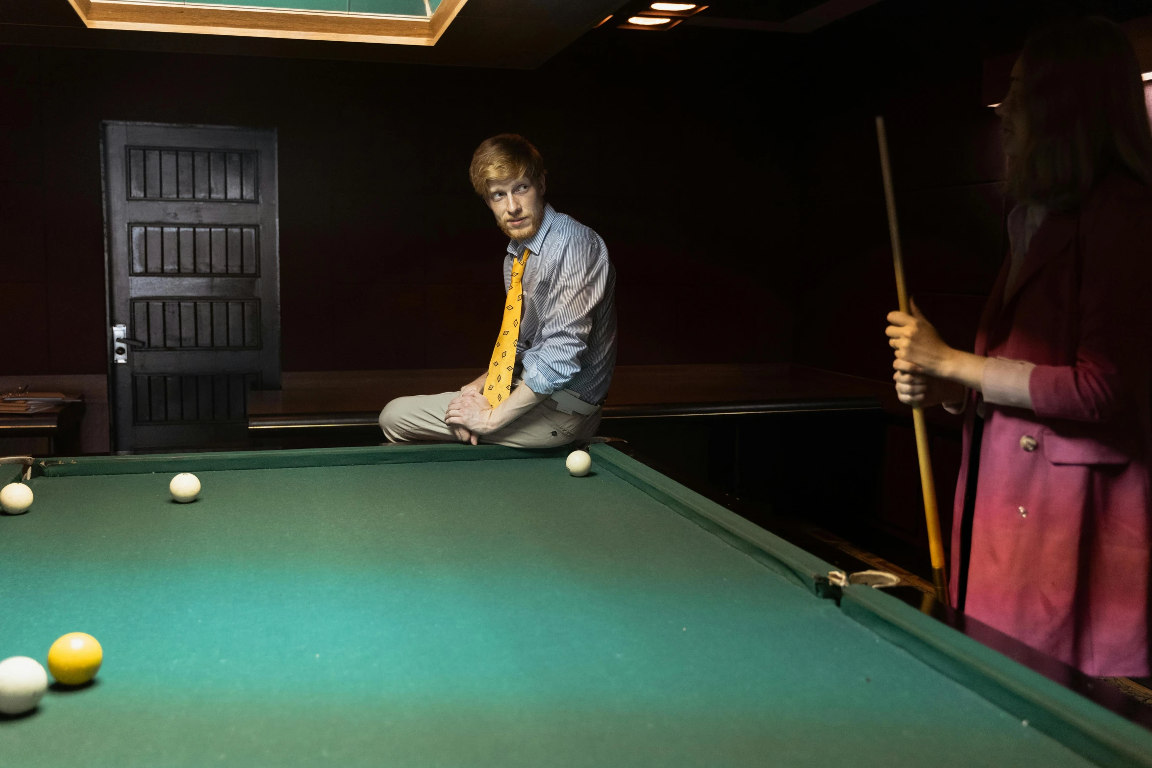two people standing around a pool table with pool balls