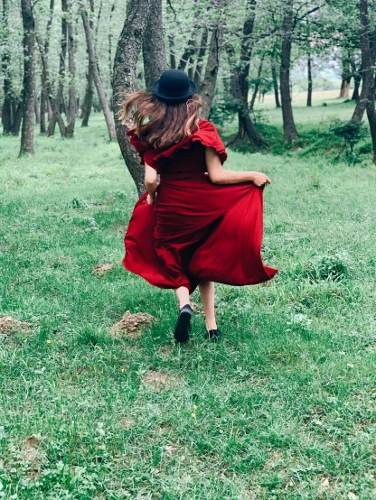 a woman in a red dress is standing in a field near a forest