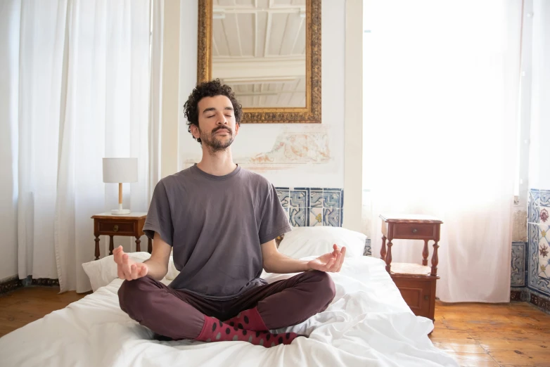 man is sitting on a bed while practicing yoga