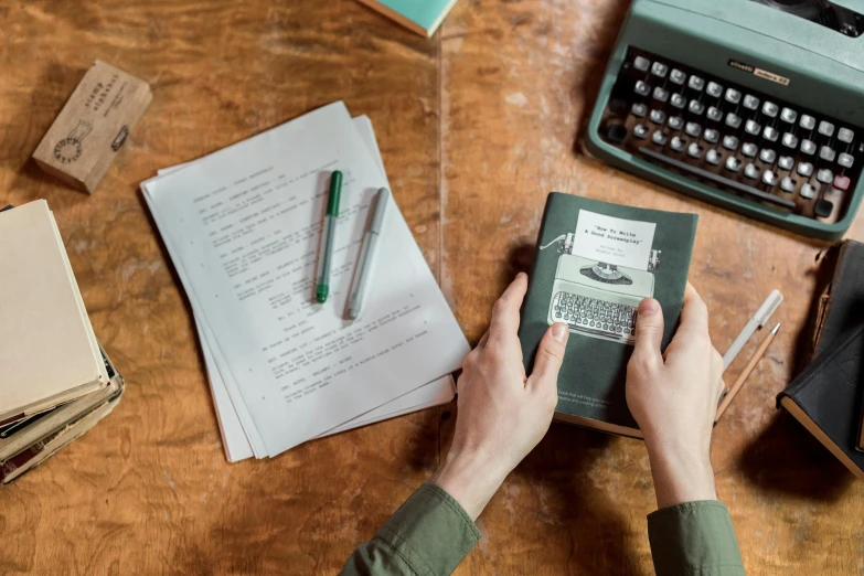 a person's hands holding up a typewriter next to paper