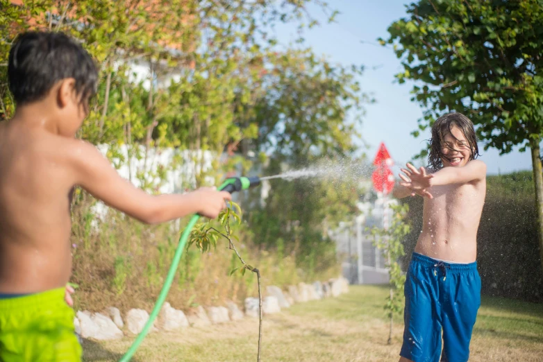 two s playing with a sprinkler and hose in the yard