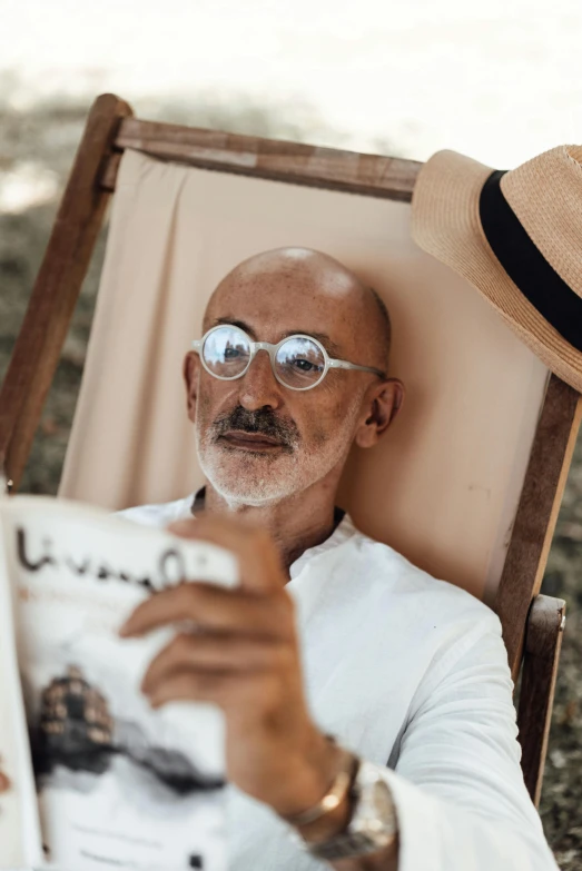 an older man wearing sunglasses, and reading the newspaper