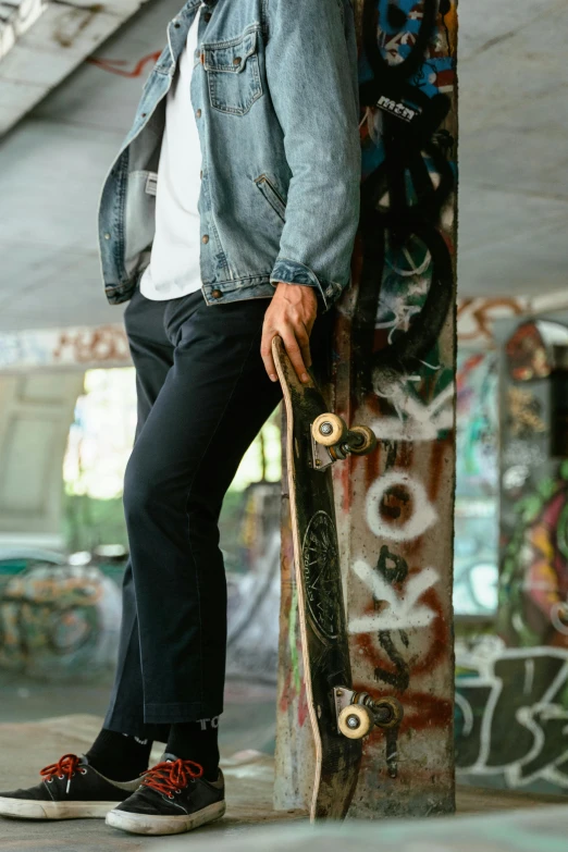 a man standing up against a tall pillar holding a skateboard