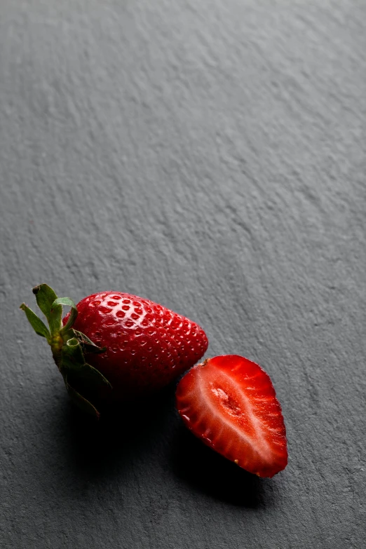 a sliced strawberry and a whole strawberry sitting on top of the floor