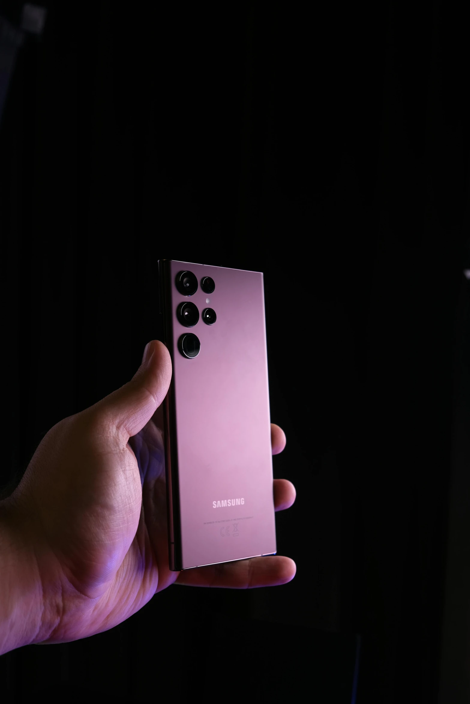 a hand holding a pink remote control in front of a black backdrop