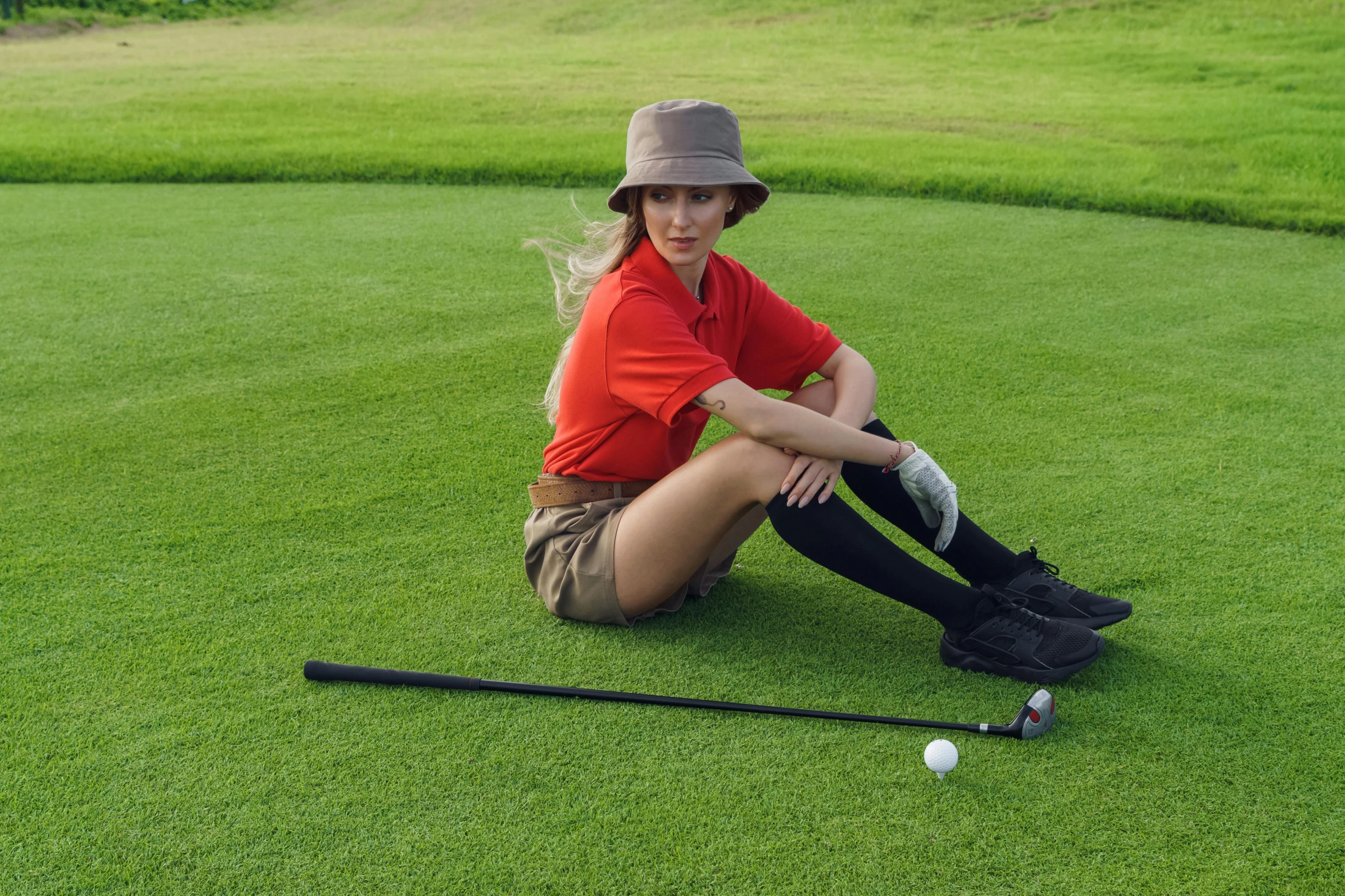 a woman sitting in the grass with a golf bat and ball