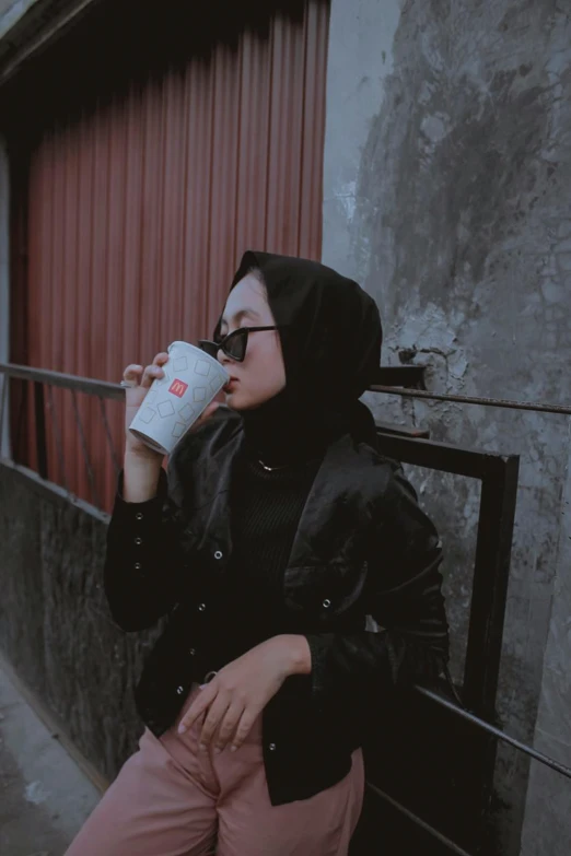 a girl with glasses wearing a black hoodie drinking from a cup