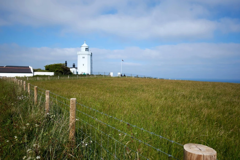 a farm area has a house and tall lighthouse in the background