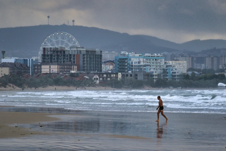 a person is walking on a beach near a ferris wheel