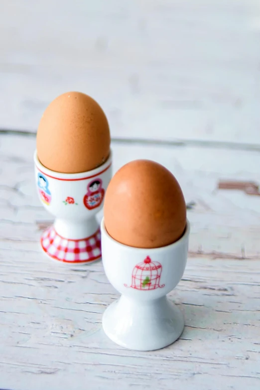 two eggs sit in a white egg holder on a wooden table