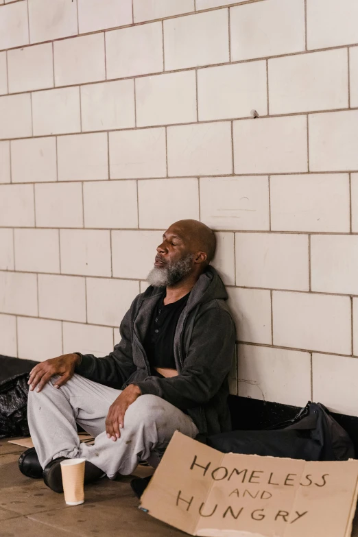 a homeless man is sitting against the wall of an urban building
