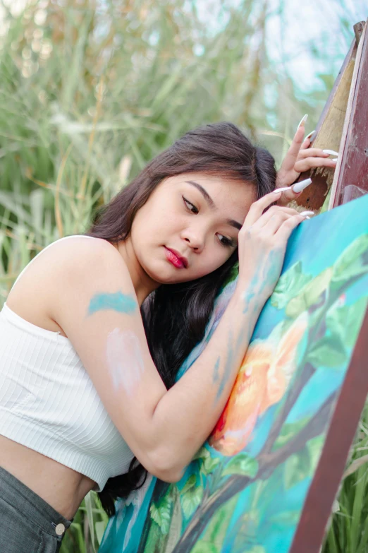 a woman holding a painting next to a brush