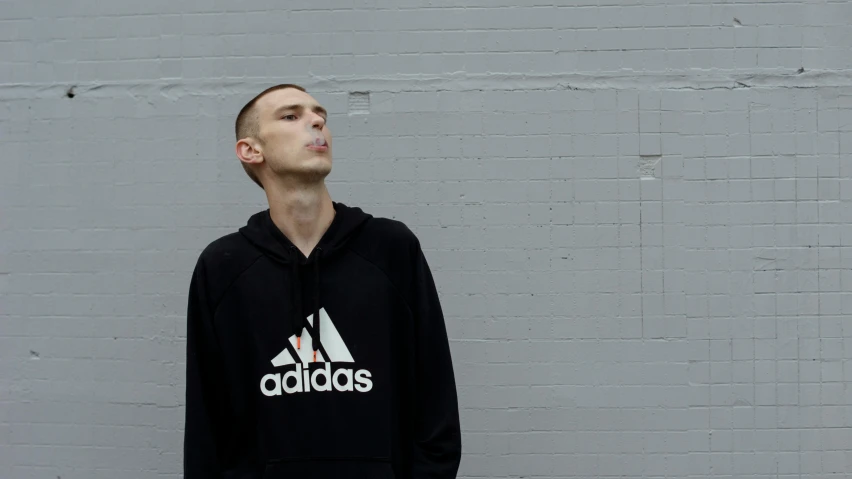 the young man stands against a gray wall