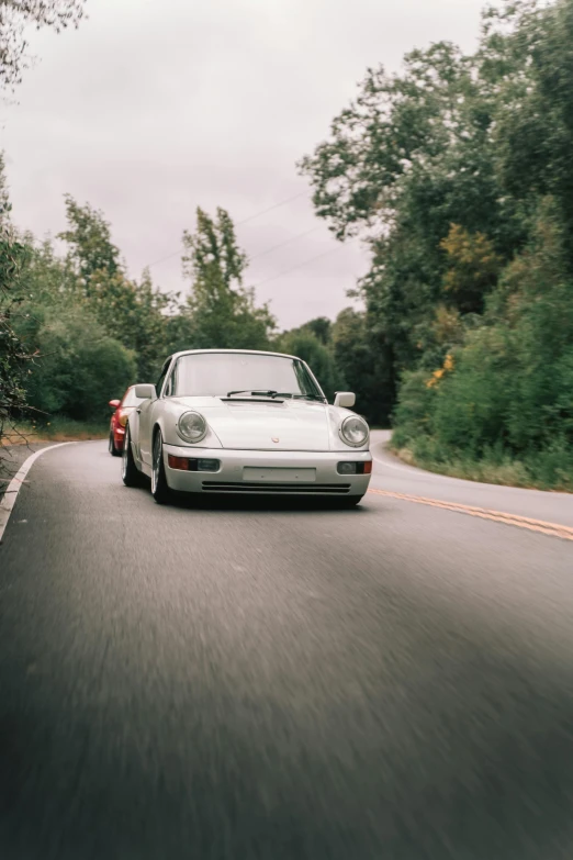 a white car driving down a road past green trees