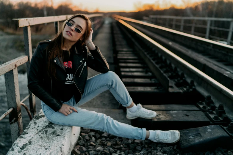 woman sitting on rail next to train tracks and sunset