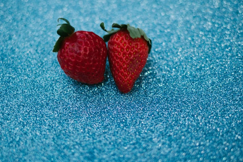 two strawberries against a blue background with small bubbles