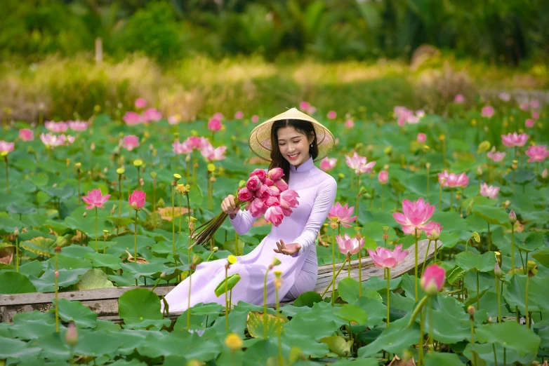 a woman in a hat holding a bouquet of flowers sitting in the middle of a water lily garden